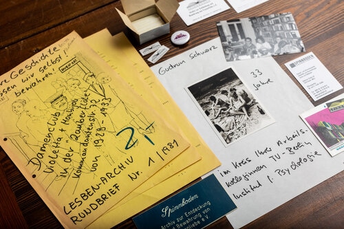 Auf dem Foto sind frühe Erzeugnisse aus der Gründungszeit des Spinnbodens abgebildet. So der erste Rundbrief von 1981 und ein Foto von Gudrun Schwar, welche das Archiv gegründet hat.