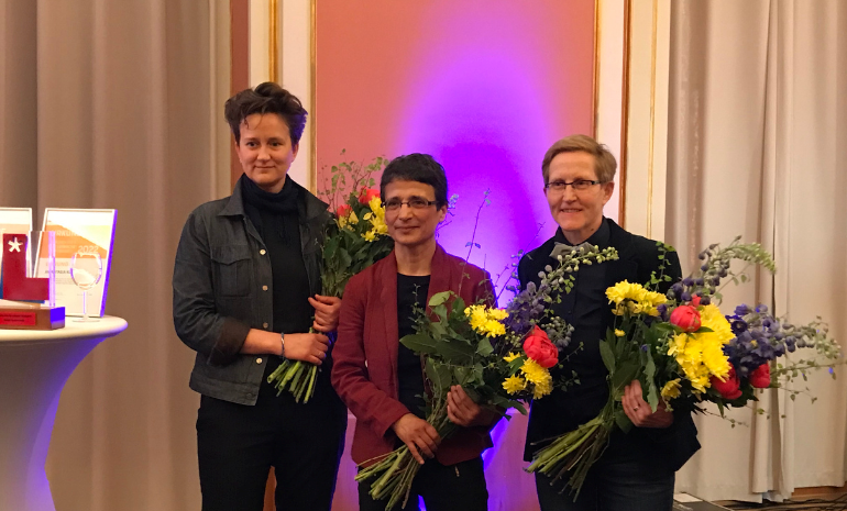 Zu sehen sind die Preisträgerin Saideh Saadat-Lendle in der Mitte und die ausgewählten Nominierten Anastasia Klevets (links) sowie Katja Koblitz (rechts). Alle halten einen Blumenstrauß in der Hand.